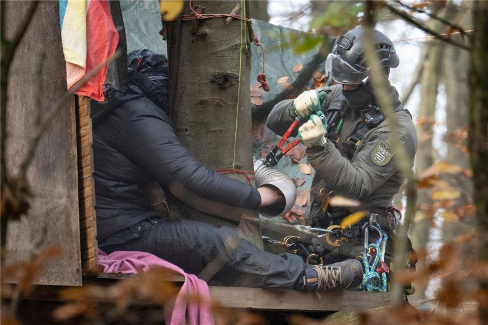 Ein Aktivist hat sich festgeklebt - ein Beamter des Höhen-Interventionsteams löst ihn ab.Boris Roessler/dpa