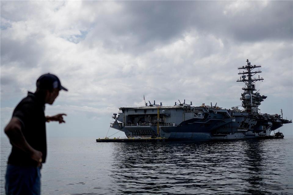 Ein Arbeiter zeigt auf den Flugzeugträger USS Nimitz der U.S. Navy, der im Golf von Panama andockt.Matias Delacroix/AP/dpa