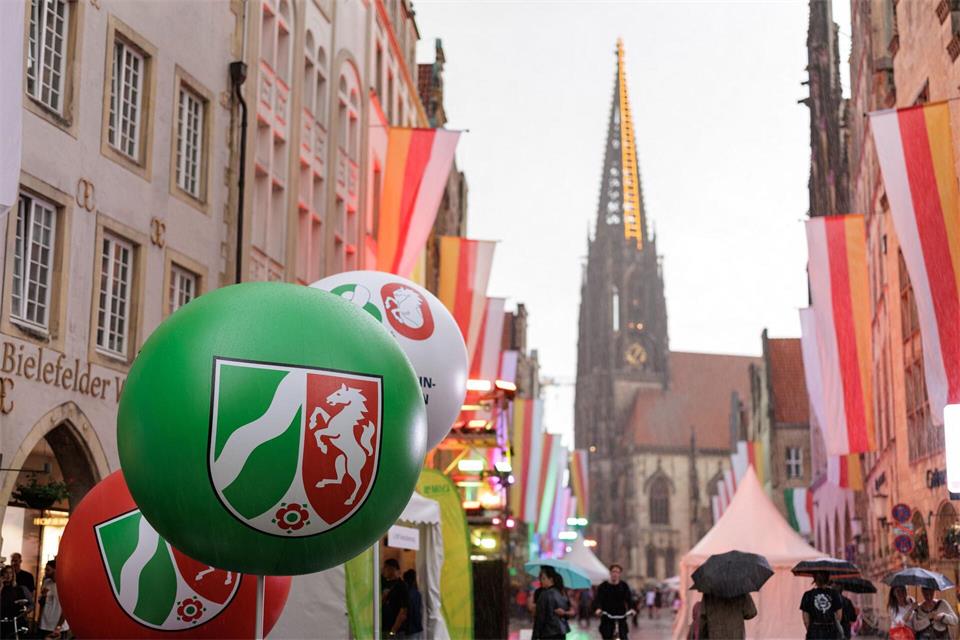 Ein Ballon mit dem NRW-Landeswappen schwebt im Rahmen der Feierlichkeiten zum 80. Landesjubiläum während eines Regenschauers über dem Prinzipalmarkt in Münster.David Ebener/dpa