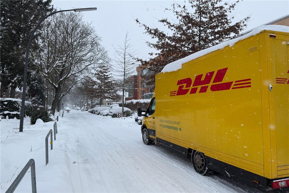 Ein DHL-Lieferfahrzeug ist auf einer verschneiten Straße im Hamburger Stadtteil Lokstedt unterwegs.Stephanie Lettgen/dpa