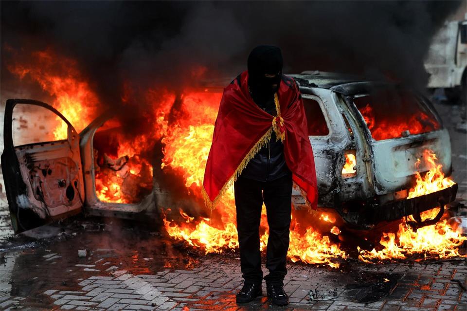 Ein Demonstrant, der sich in eine albanische Flagge gehüllt hat, steht während einer regierungskritischen Demonstration in Tirana vor dem Büro des Ministerpräsidenten vor einem brennenden Auto.Hameraldi Agolli/AP/dpa