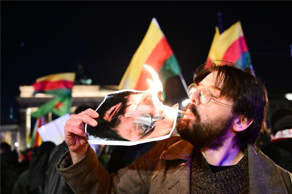 Ein Demonstrant zündet sich während einer Demonstration eine Zigarette an dem Bild des syrischen Präsidenten an.Sebastian Christoph Gollnow/dpa