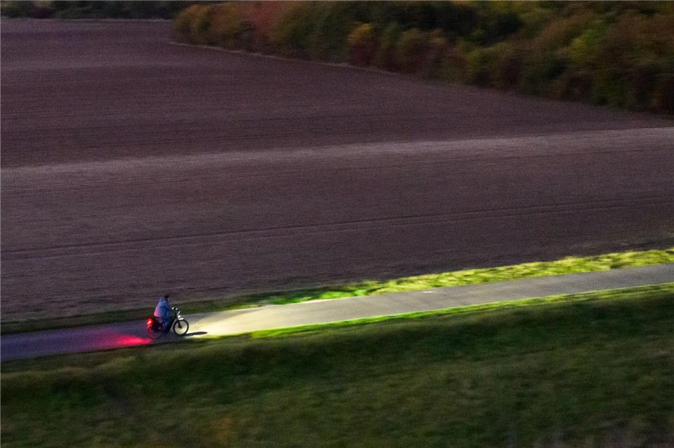 Ein Fahrradfahrer fährt am frühen Morgen mit Licht über einen Feldweg bei Hannover.Julian Stratenschulte/dpa