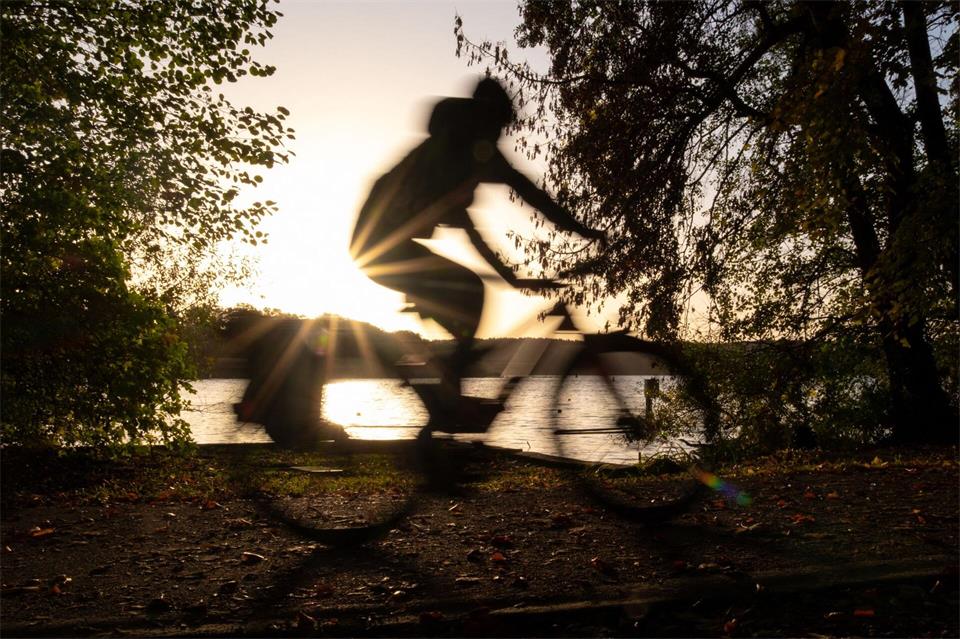 Ein Fahrradfahrer fährt bei Sonnenaufgang am Ufer des Templiner Sees entlang.Georg-Friedrich Moritz/dpa