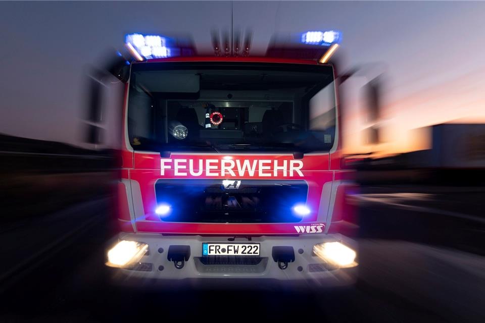 Ein Feuerwehrfahrzeug steht mit eingeschaltetem Blaulicht im Sonnenuntergang auf einer Straße.