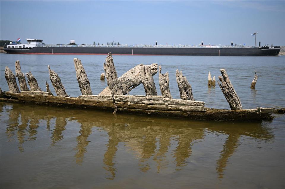 Ein Frachtschiff fährt bei Niedrigwasser auf dem Rhein an dem „Gerippe“ eines Bootes vorbei.Federico Gambarini/dpa