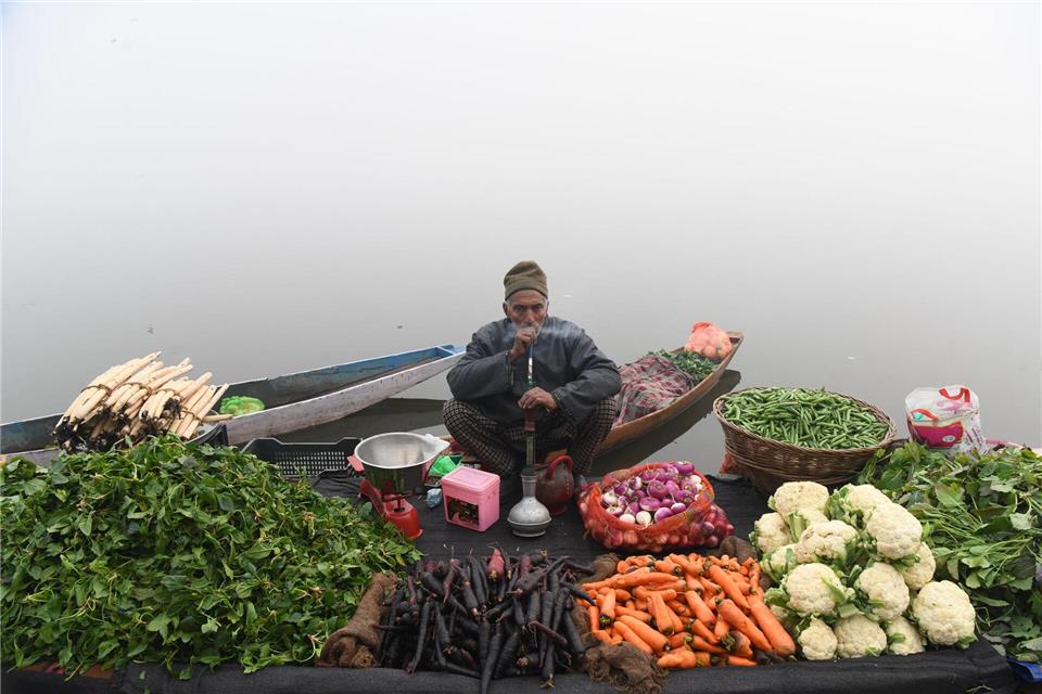 Ein Gemüsehändler raucht eine Wasserpfeife, während er an einem nebligen Tag am Ufer eines Sees im indischen Srinagar auf Kunden wartet.Basit Zargar/ZUMA Press Wire/dpa