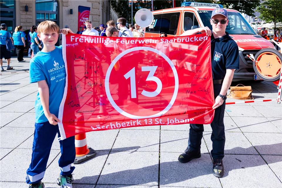 Ein Jugendfeuerwehrmann (l.) und ein aktiver Feuerwehrmann der Freiwilligen Feuerwehr Saarbrücken-St. Johann (LB 13) präsentieren ein besonderes Banner mit der Zahl 13.Laszlo Pinter/dpa