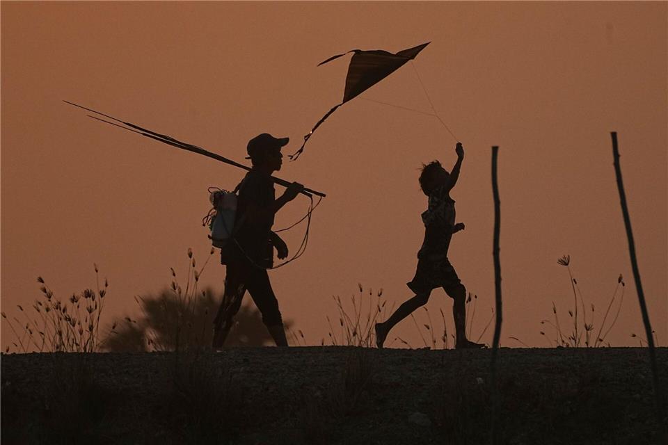 Ein Junge (r) lässt einen Drachen steigen, während er mit seinem Vater nach dem Fischen am Stadtrand von Phnom Penh nach Hause geht.Heng Sinith/AP/dpa