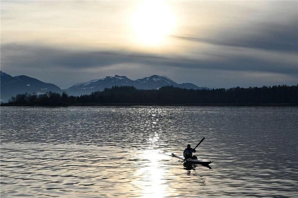Ein Kajakfahrer fährt vor schneebedeckten Bergen über den Chiemsee.Katrin Requadt/dpa