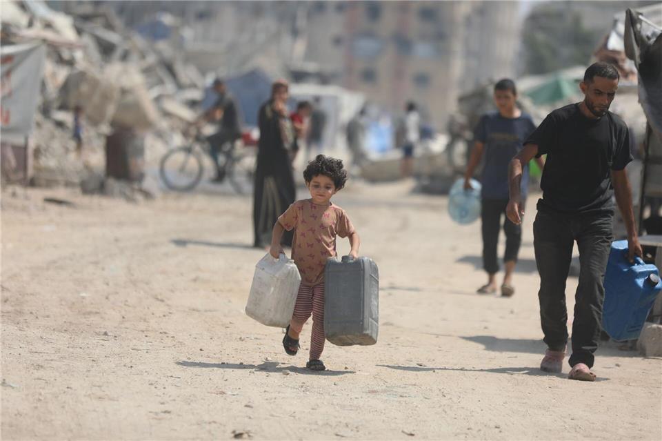 Ein Kind trägt Kanister, um sich in Gaza Wasser von einem Tankwagen zu holen.Omar Ashtawy/APA Images via ZUMA Press Wire/dpa
