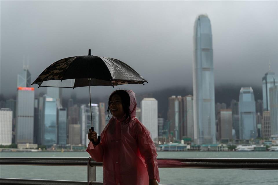 Ein Mädchen hält einen Regenschirm in Tsim Sha Tusi vor dem Victoria Harbor und der Skyline von Hongkong während des Taifuns „Tapah“.Vernon Yuen/Nexpher via ZUMA Press Wire/dpa