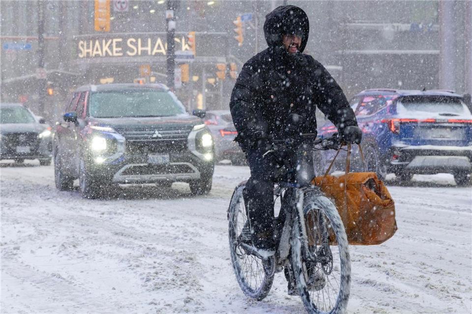 Ein Mann fährt an einem verschneiten Tag in Toronto auf einem E-Bike.Zou Zheng/XinHua/dpa
