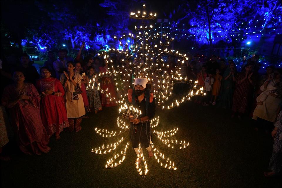 Ein Mann hält in einem mit Öllampen geschmückten Kostüm in der fünften Nacht von Navratri, dem Fest der neun Nächte, das Aarti-Ritual ab.Ajit Solanki/AP/dpa