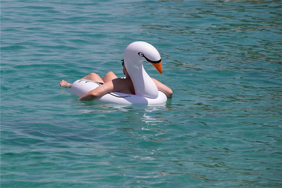 Ein Mann lässt sich auf einem Schwimmtier am Strand von Cala Vinyes auf Mallorca im türkisblauen Wasser treiben.Clara Margais/dpa
