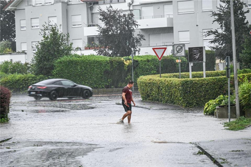 Ein Mann läuft in Friedrichshafen am Bodensee durch eine tiefe Pfütze.Jason Tscheppljakow/dpa
