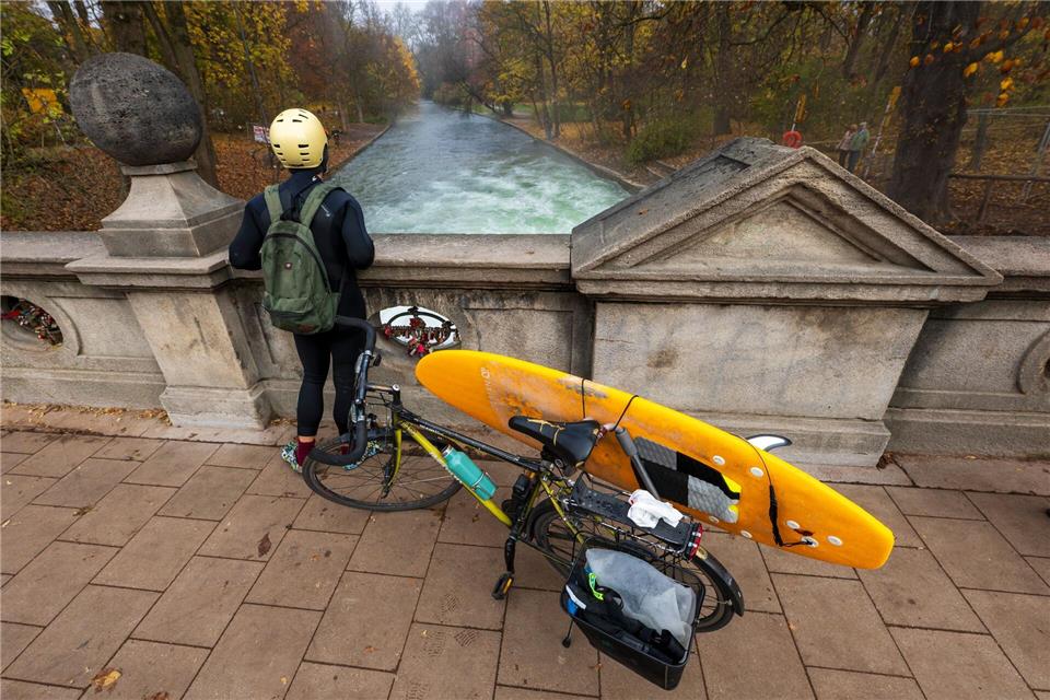 Ein Mann mit einem Surfboard an seinem Fahrrad schaut von einer Brücke auf die - nicht mehr vorhandene - Eisbachwelle im Englischen Garten.Peter Kneffel/dpa