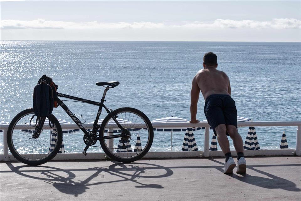 Ein Mann mit nacktem Oberkörper macht am Strand von Nizza neben seinem Fahrrad Übungen. (Archivbild)Serge Haouzi/XinHua/dpa