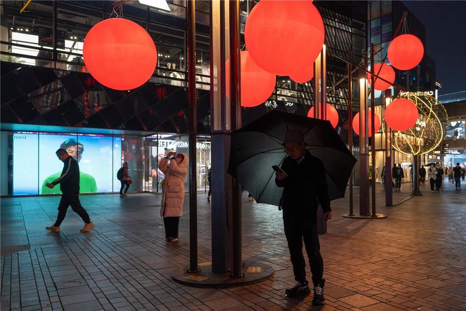 Ein Mann schaut auf sein Telefon in der Nähe von roten Zierkugeln am Taikoo Li Sanlitun Einkaufszentrum in Peking.Ng Han Guan/AP/dpa