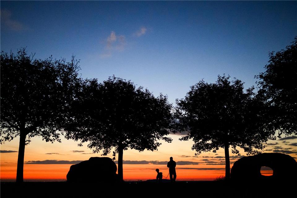 Ein Mann spaziert am frühen Morgen kurz vor Sonnenaufgang mit einem Hund über den Kronsberg.Julian Stratenschulte/dpa