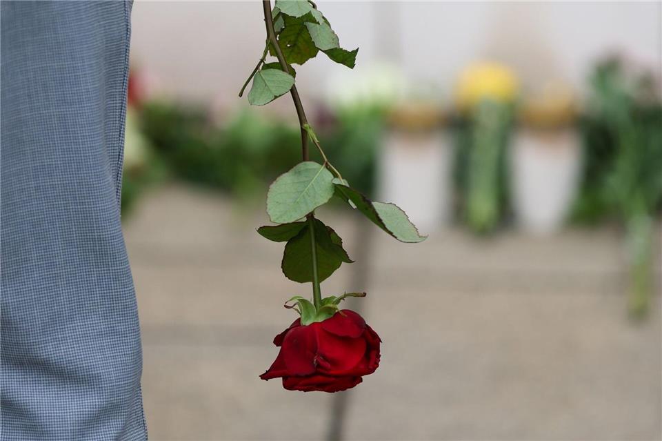 Ein Mann steht mit einer Rose in der Hand vor Blumen und Kerzen am Paulinum der Universität Leipzig.Jan Woitas/dpa