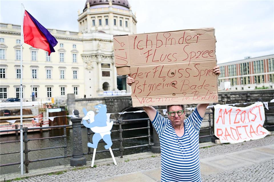 Ein Mann steht während der Schwimm-Demonstration gegen das Badeverbot in der Spree mit einem Schild am Ufer.Sebastian Christoph Gollnow/dpa