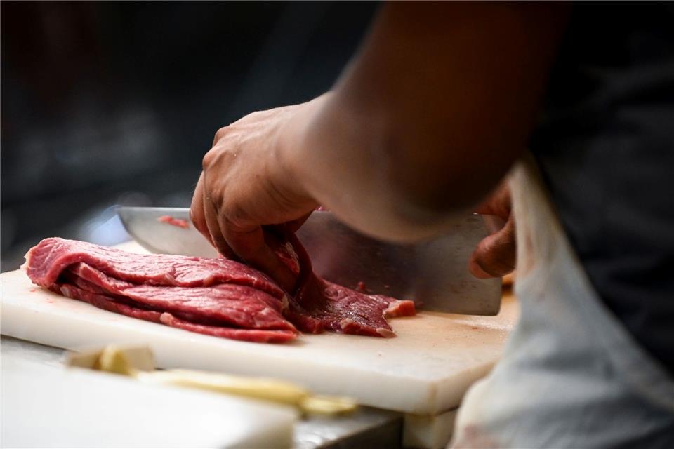 Ein Metzger schneidet Fleisch an der Theke seines Lokals.