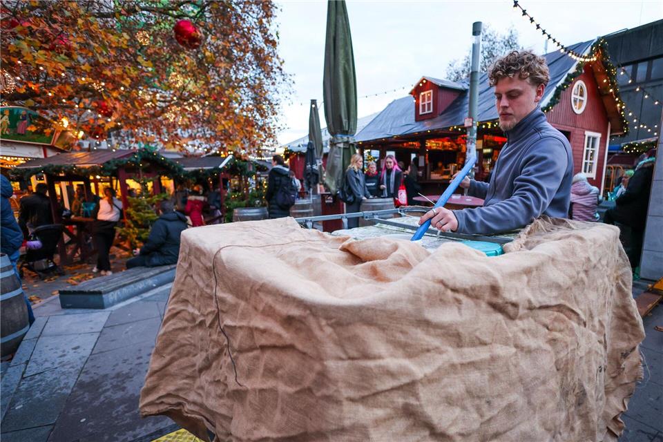 Ein Mitarbeiter eines kleinen Weihnachtsmarkts befüllt einen Kunststofftank mit Wasser und verkleidet ihn mit Stoff.Christian Charisius/dpa