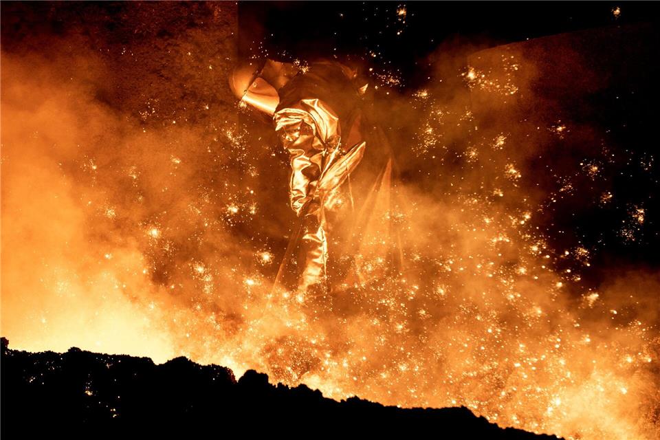 Ein Mitarbeiter reinigt in einem Stahlwerk die Abstichrinne am Hochofen.Hauke-Christian Dittrich/dpa