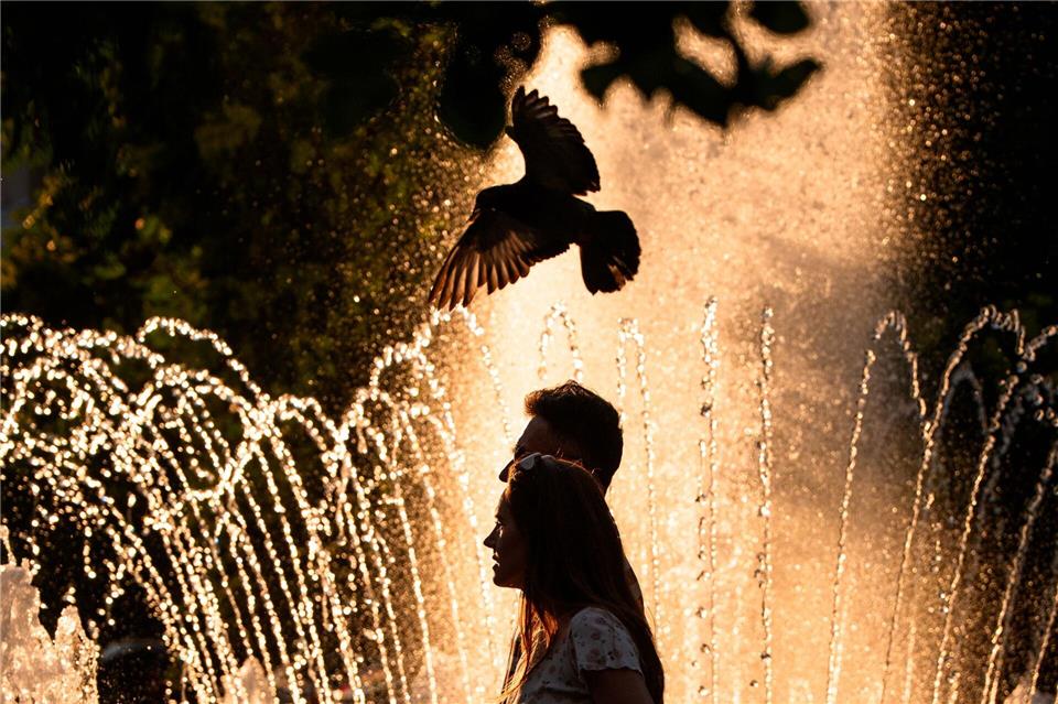 Ein Paar geht an einem Springbrunnen in Bukarest vorbei, während der nationale Wetterdienst für Teile des Landes in den kommenden Tagen eine Hitzewarnung der Stufe „Rot“ herausgegeben hat.Andreea Alexandru/AP/dpa