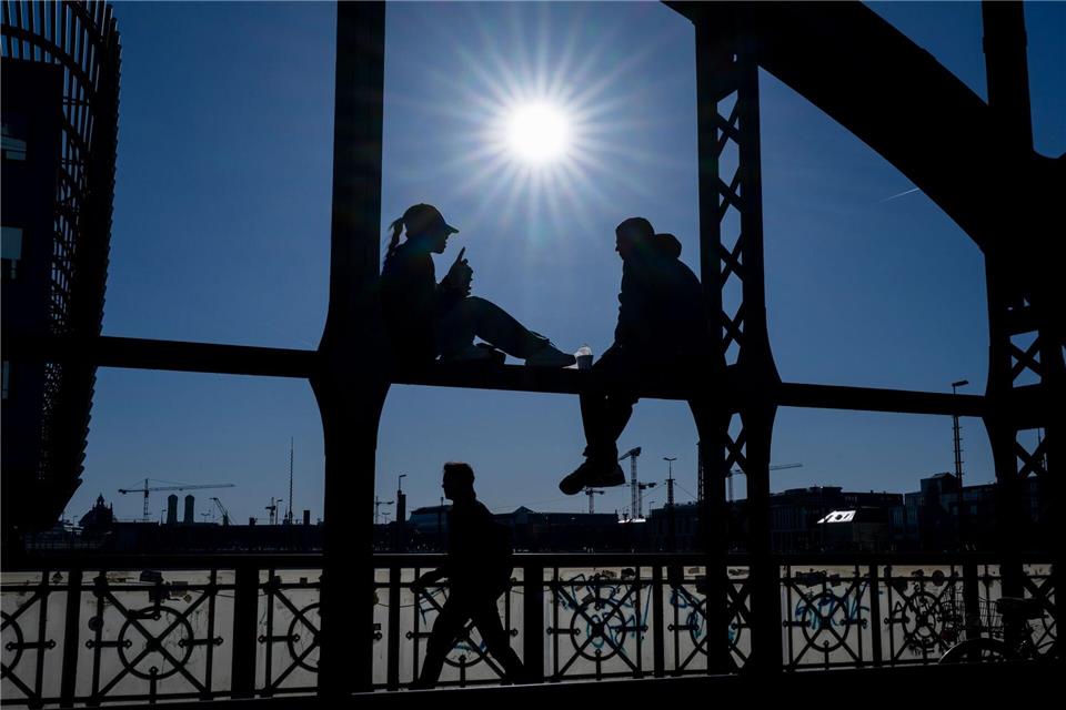 Ein Pärchen sitzt in der Sonne auf dem Geländer der Hackerbrücke in München. Peter Kneffel/dpa