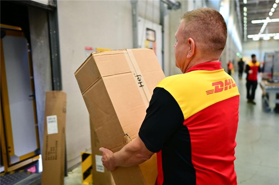 Ein Paketbote schleppt in einem DHL-Standort ein schweres Paket. (Archivbild)Sebastian Christoph Gollnow/dpa