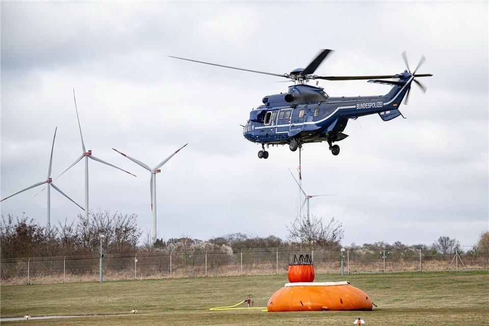 Ein Polizeihubschrauber nimmt über einen Außenbehälter Wasser aus einem Tank. Fabian Sommer/dpa