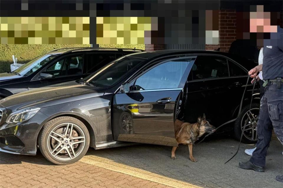 Ein Polizist mit Spürhund durchsucht einen Mercedes unter einem Carport in Bocholt. Die Aufnahme entstand während der Drogenrazzia im April 2026.