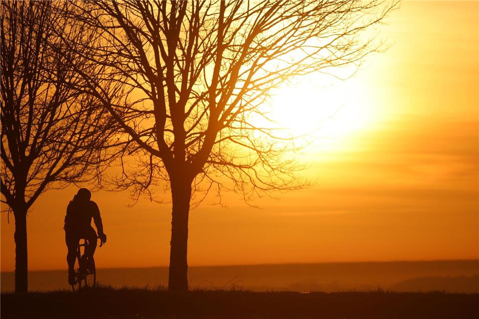 Ein Radfahrer ist am Morgen kurz nach Sonnenaufgang unterwegs, während sich der Himmel durch den Saharastaub in Orangetönen verfärbt hat.Thomas Warnack/dpa