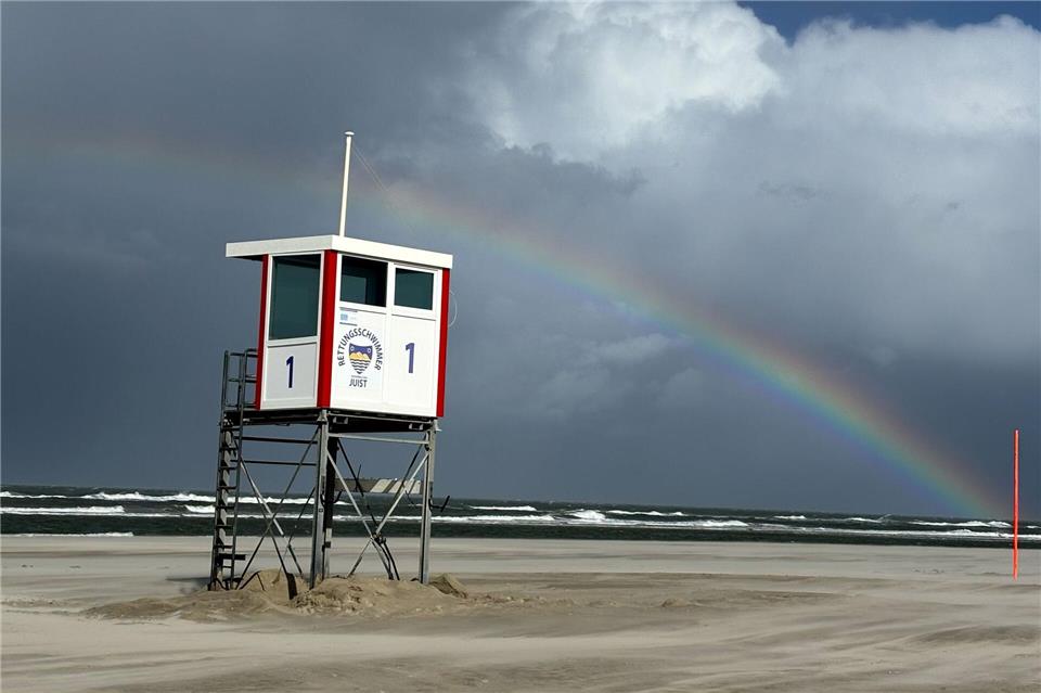 Ein Regenbogen steht an einem Himmel voll dunkler Wolken über der Nordsee und über der Insel Juist. Federico Gambarini/dpa