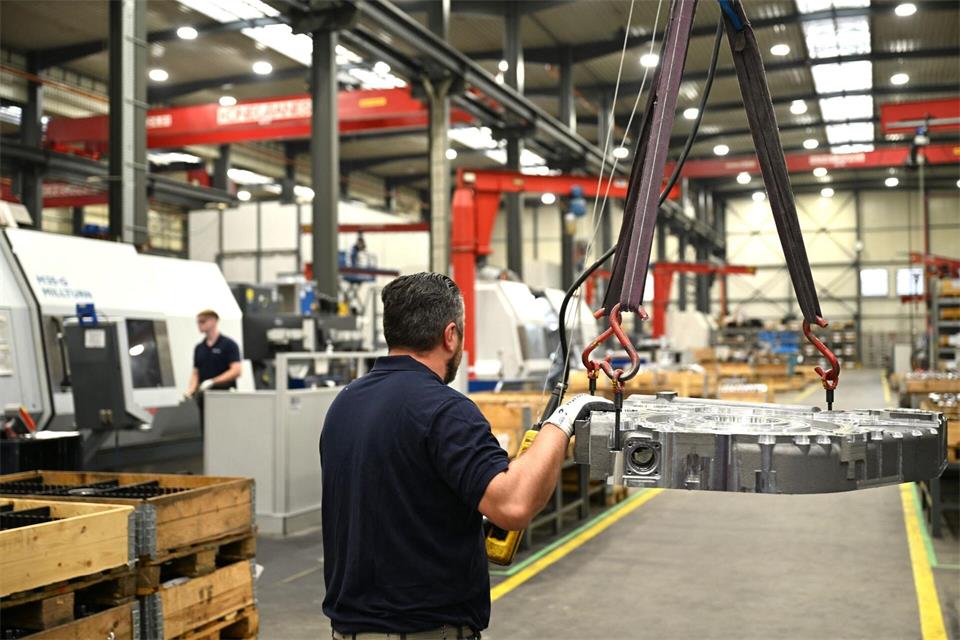 Ein Renk-Mitarbeiter hievt eine Getriebeplatte mit einem Kran hoch. Im Hintergrund links in Weiß sind neue Maschinen zu sehen, mit denen Getriebebauteile deutlich schneller bearbeitet werden können als früher. Wolf von Dewitz/dpa