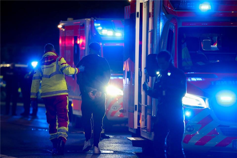 Ein Tatverdächtiger in Handschellen wird nach Schüssen in Mönchengladbach von einem Sanitäter zu einem Rettungswagen gebracht.Christoph Reichwein/dpa