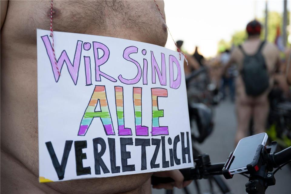 Ein Teilnehmer der Fahrrad-Demo „World Naked Bike Ride (WNBR) Berlin 2026“ trägt ein Plakat mit der Aufschrift „Wir sind alle verletzlich“. Christophe Gateau/dpa
