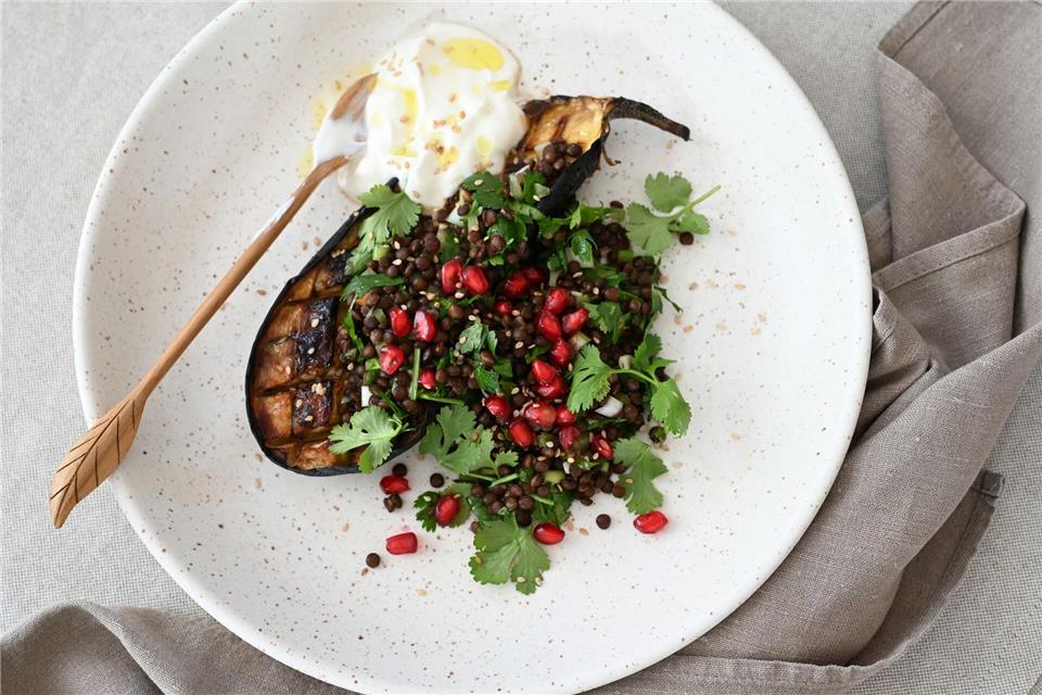 Ein Teller voller Kontraste und orientalischem Twist: Geschmorte Auberginen, getoppt mit Linsen-Kräuter-Salat, Granatapfelkernen und einem Klecks cremigem Joghurt.Julia Uehren/dpa-tmn