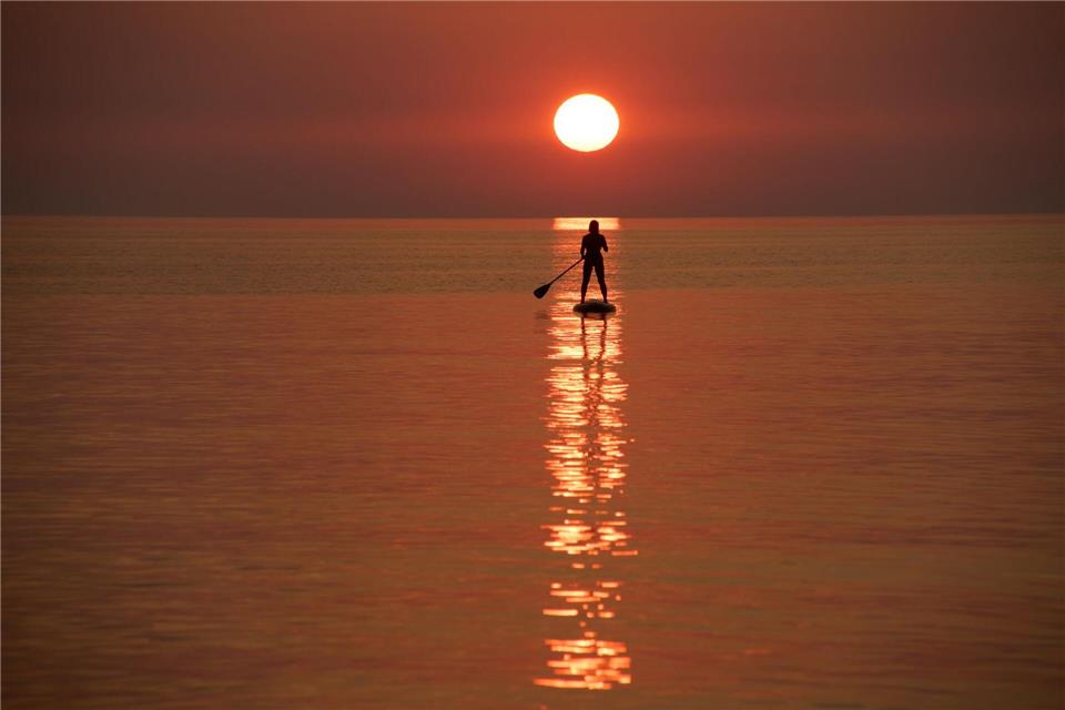 Ein Urlauber steuert bei Sonnenuntergang vor der Küste von Jantarny dem früheren ostpreußischen Palmnicken, einem Ferienort in der westrussischen Region Kaliningrad, ein Stand-up-Paddleboard.Alexander Zemlianichenko/AP/dpa
