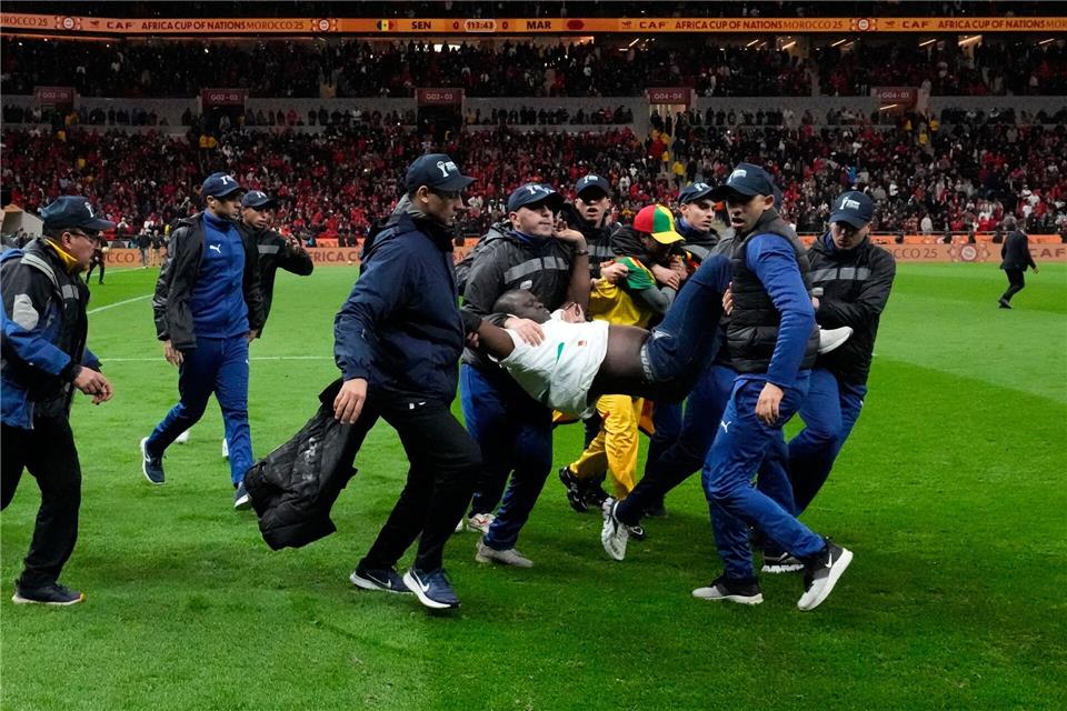 Ein auf das Spielfeld gestürmter Anhänger des Senegal wird von Sicherheitskräften vom Platz getragen. (Archivbild)Themba Hadebe/AP/dpa