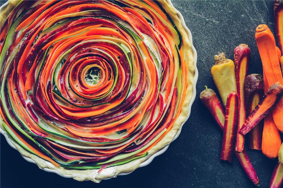 Ein echter Hingucker: Gehobelte Streifen von orangen, gelben und lila Möhren sowie einer Zucchini spiralförmig auf einem Mürbeteigboden mit Eier-Ziegenkäsegemisch legen und backen - fertig ist die Tarte.Aileen Kapitza/minzgruen.com/dpa-tmn