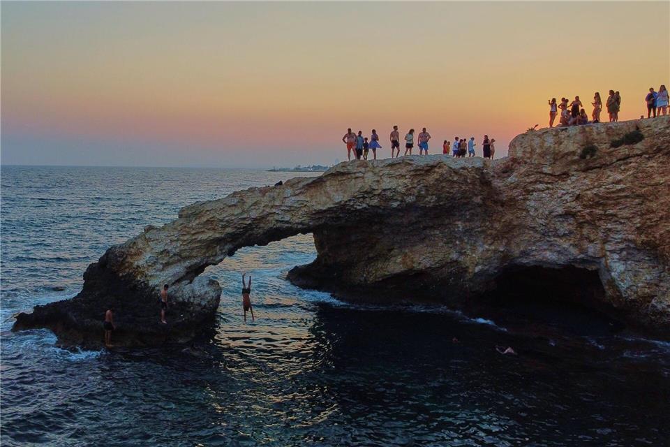 Ein junger Mann springt bei Sonnenuntergang im Ferienort Ayia Napa auf der im östlichen Mittelmeer gelegenen Insel Zypern von der natürlichen „Liebesbrücke“ ins Meer.Petros Karadjias/AP/dpa