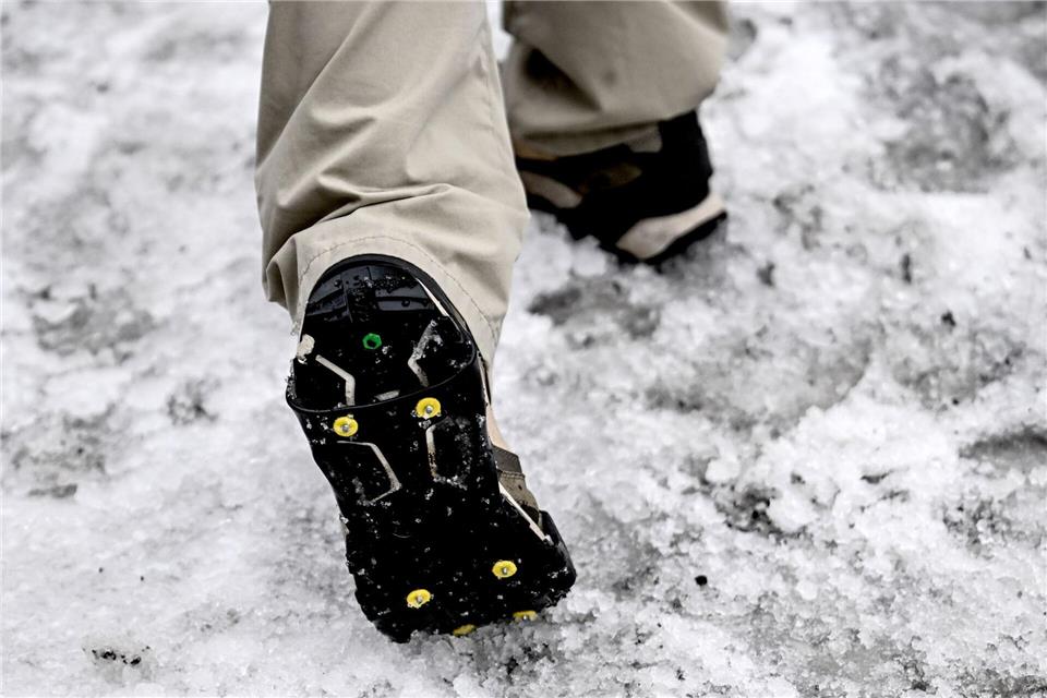 Ein junger Mann trägt Spikes im Schneematsch an den Schuhen.Britta Pedersen/dpa