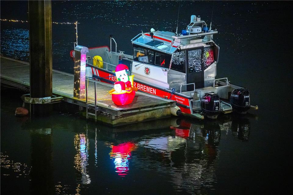 Ein leuchtender Weihnachtsmann steht neben einem Boot der Feuerwehr an der Weser in Bremen. Sina Schuldt/dpa