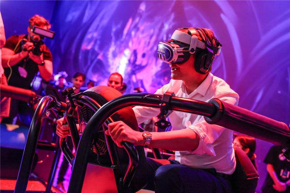 Ein wilder Ritt bei der Gamescom 2024: Hendrik Wüst auf einem „Drachen“, genauer gesagt mit virtueller Brille auf einem schwankenden Gestell.Oliver Berg/dpa