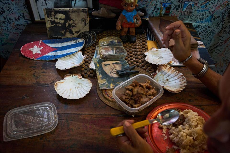 Eine Angestellte eines Souvenirgeschäfts in Havanna isst neben Bildern von Che Guevara, Fidel Castro und Ernest Hemingway.Ramon Espinosa/AP/dpa