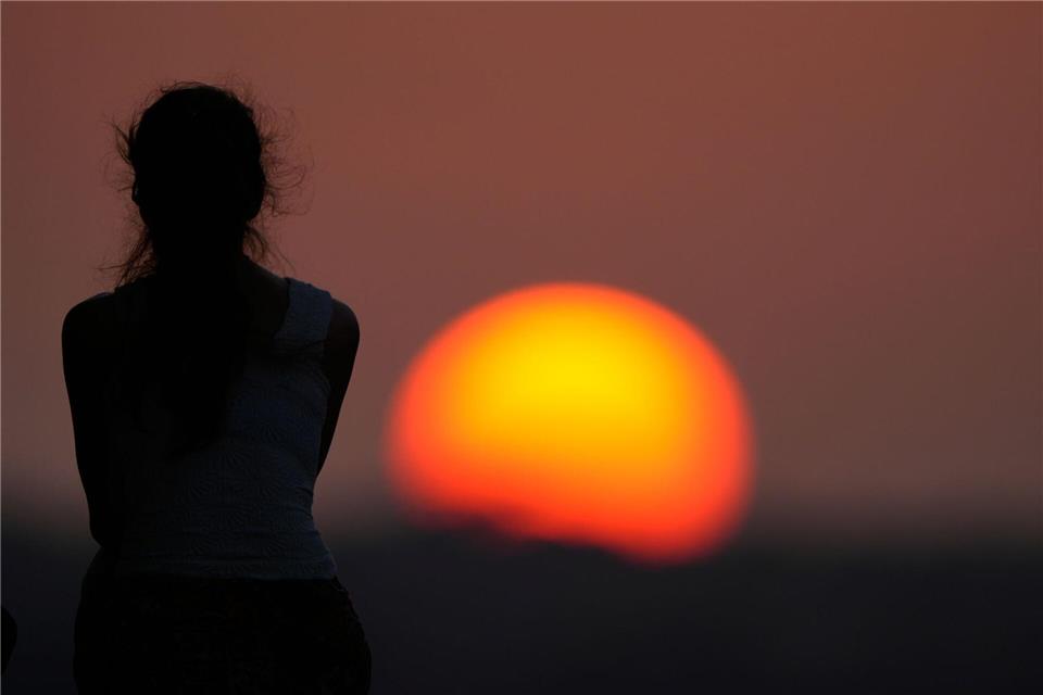Eine Frau beobachtet den Sonnenuntergang.Charlie Riedel/AP/dpa