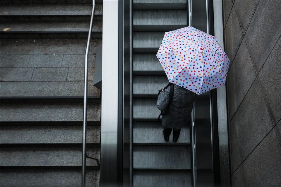 Eine Frau fährt mit ihrem Regenschirm eine Rolltreppe hinauf. Das Wetter soll in der Region Stuttgart in den nächsten Tagen wechselhaft bleiben.Christoph Schmidt/dpa